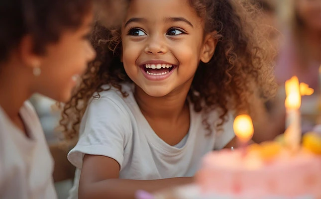 Smiling young girl celebrating her birthday with candles on a cake, surrounded by friends in a joyful setting.